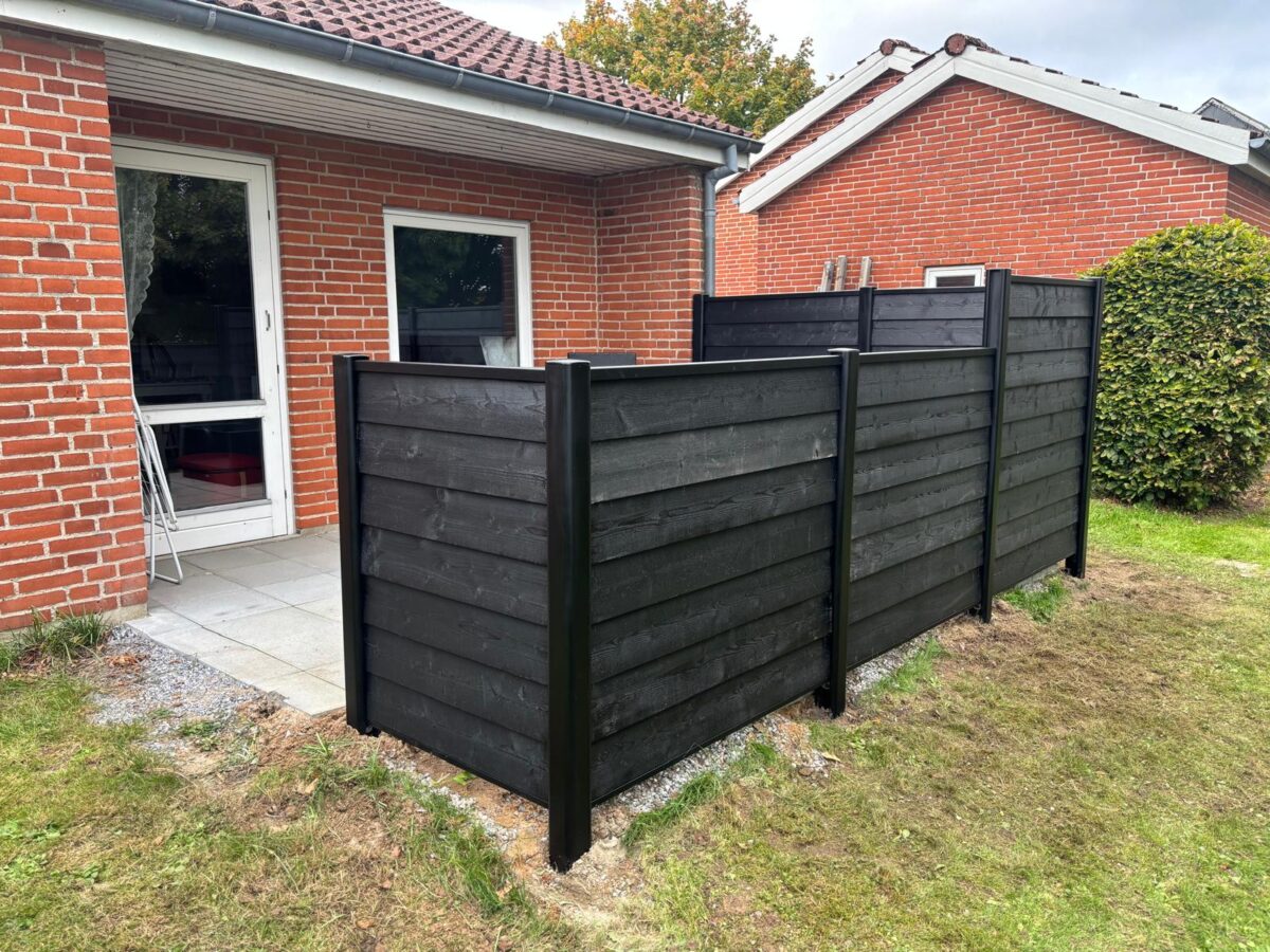 Sort træskærm med vandrette brædder i alustolper omkring terrassen
