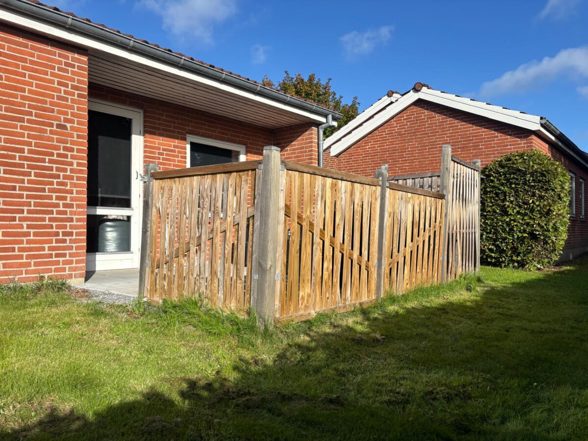 Nedslidt træhegn ved rødstenshus før udskiftning